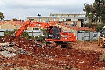 A large orange excavator is moving dirt on a construction site.