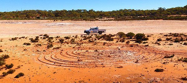 A white truck is parked in the middle of a dirt field.