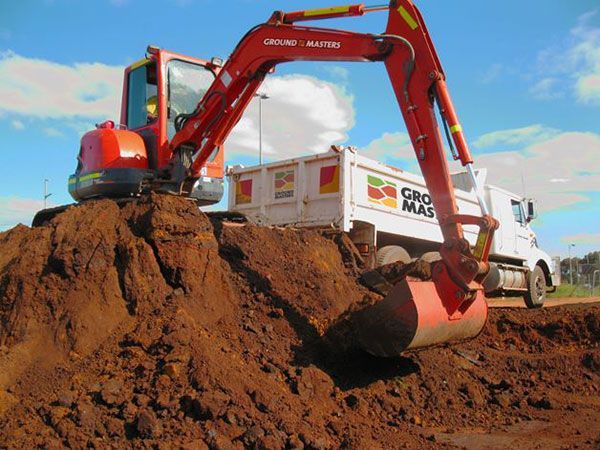 An excavator is loading dirt into a dump truck that says ground masters