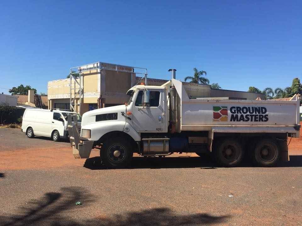 A white dump truck from ground masters is parked in a parking lot.