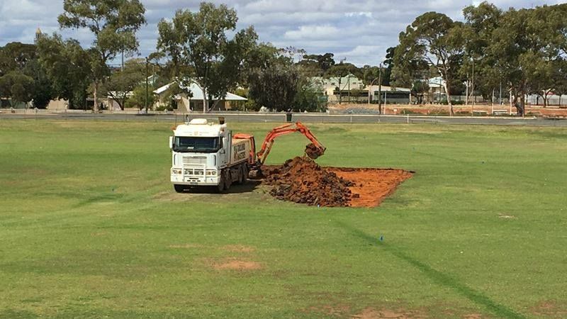 A white truck is digging a hole in a grassy field.