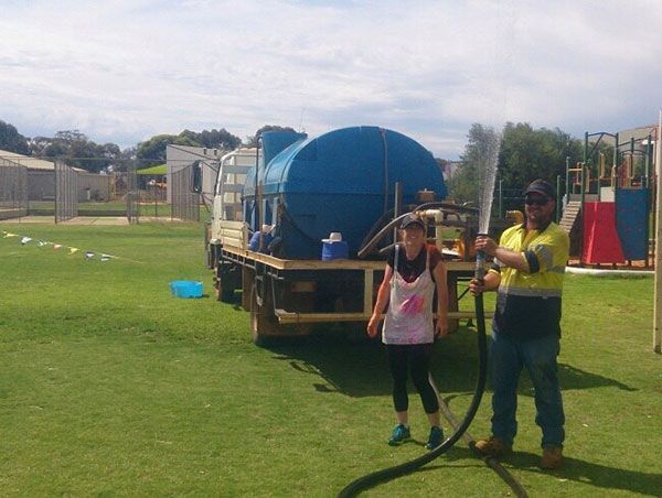 A man and a woman are standing in front of a blue tank truck.