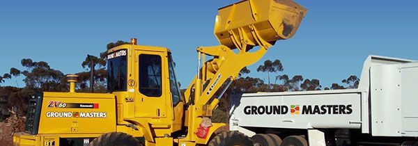 A yellow bulldozer is loading dirt into a dump truck.
