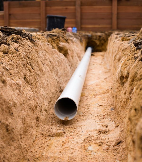 A white pipe is sitting in the middle of a dirt trench.