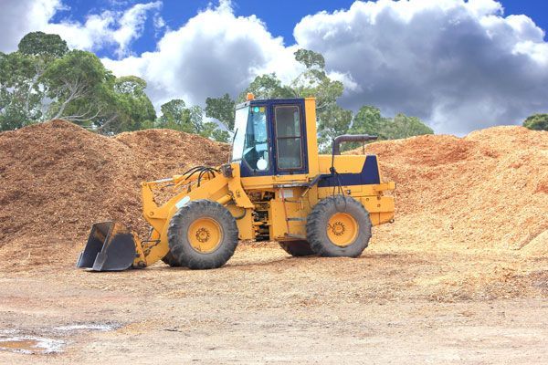 A yellow bulldozer is parked in front of a pile of wood chips.