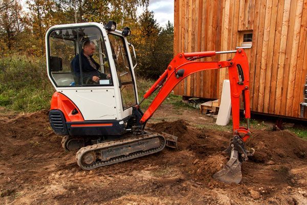 A man is driving a small excavator in a dirt field.
