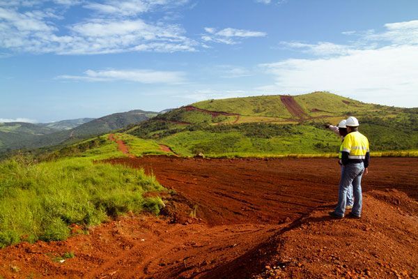 A man is standing on a dirt road looking at a mountain.