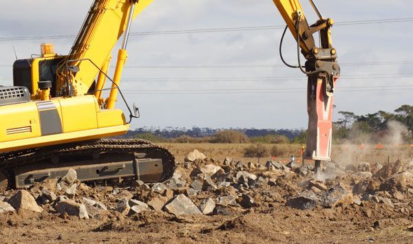 A yellow excavator is breaking rocks in a field.