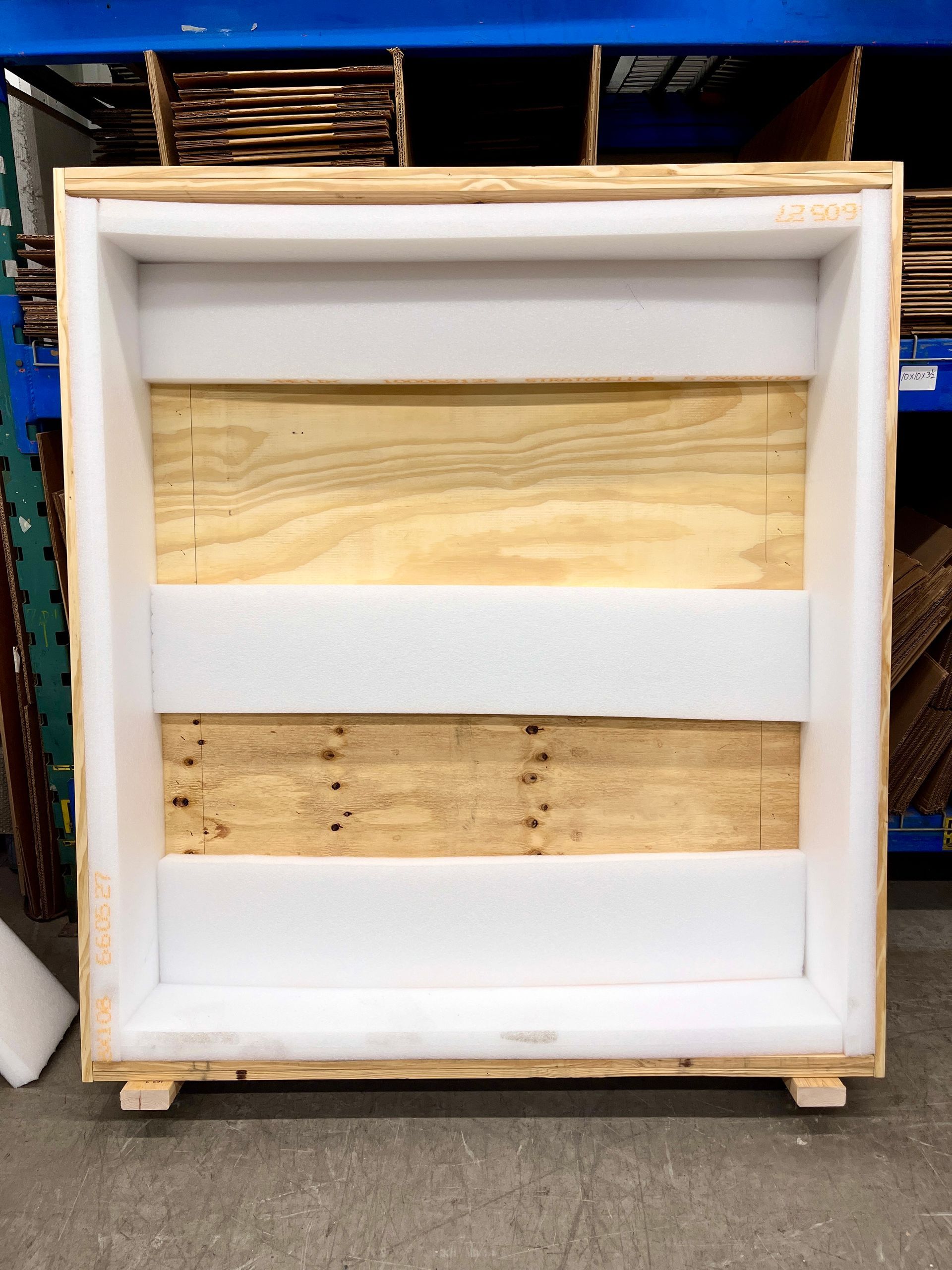 A crate, its front open, lined with foam, ready for the wrapped sign to be placed inside