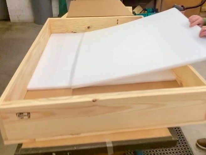 A plywood crate with a person beginning to put foam inside it