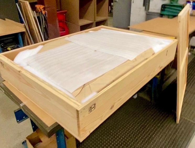 An item wrapped in protective paper, inside a plywood crate