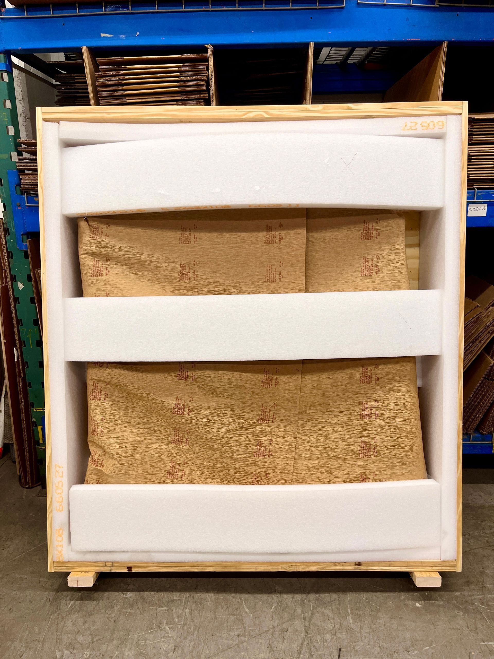 A crate, its front open, lined with foam, the wrapped sign inside and more foam planks added in front of the wrapped sign. The foam planks are arranged to be flush with the front once it is put on.