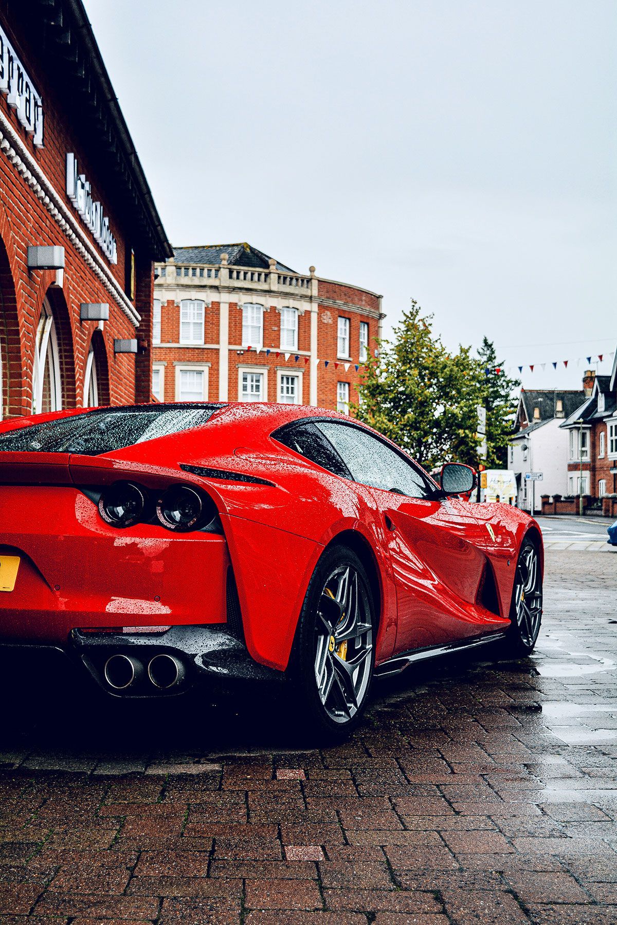 Red Ferrari sports car parked on a wet brick street in front of a building.