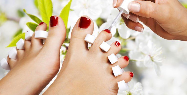 Einer Frau werden die Füße mit rotem Nagellack lackiert.