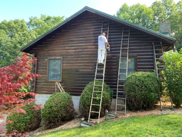 A Man Is Painting A Log Cabin With A Ladder – Boone, NC – A Brush Above Painting