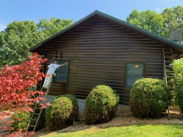 Man Painting The Side Of A Log Cabin – Boone, NC – A Brush Above Painting