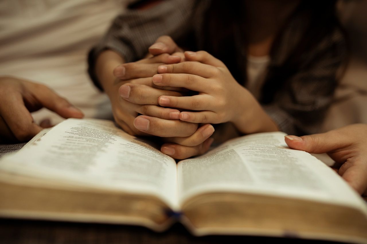 A woman and child are praying over an open bible.