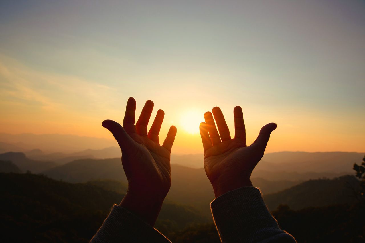 A person is reaching out their hands towards the sun at sunset.