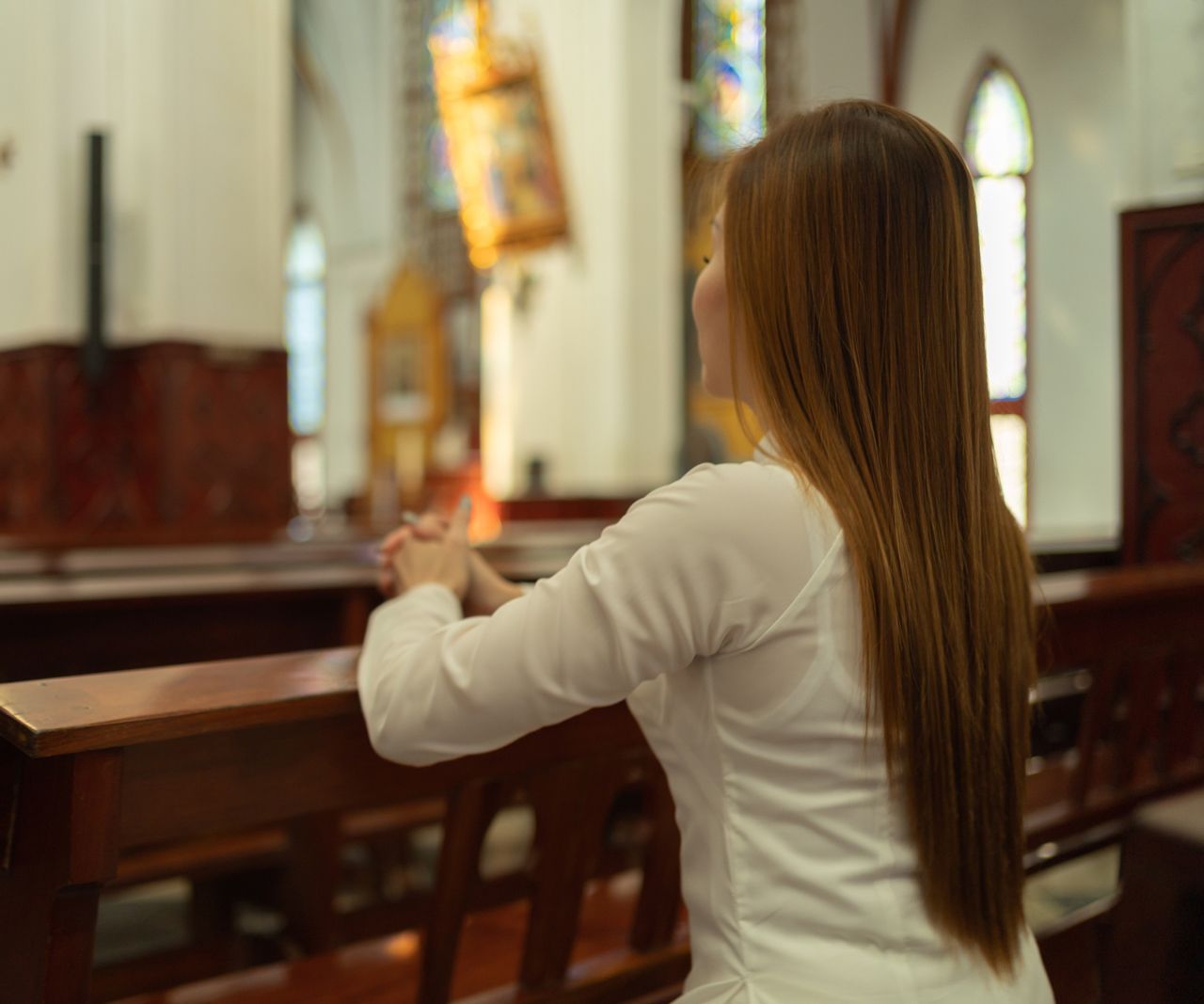 A woman is praying in a church with her hands folded.