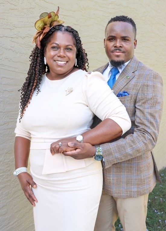 A man and a woman are posing for a picture in front of a brick wall.