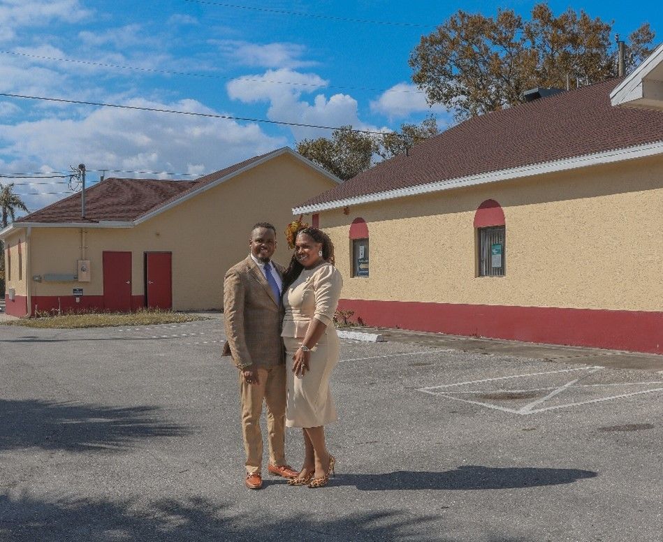 A man and a woman are standing in front of a building in a parking lot.
