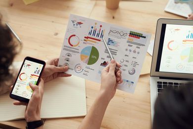 Hands reviewing colorful business charts and graphs at a wooden desk with a laptop and phone