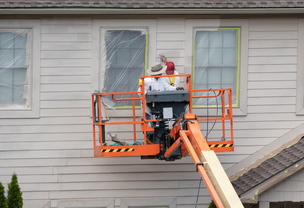 two men are painting the side of a house