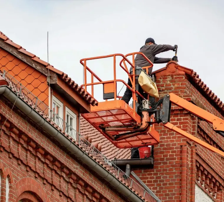 A worker in a lift basket repairing the brick roof of an old building.