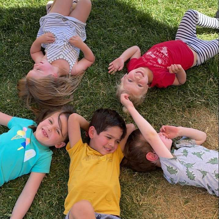 A group of children are laying in the grass in a circle.