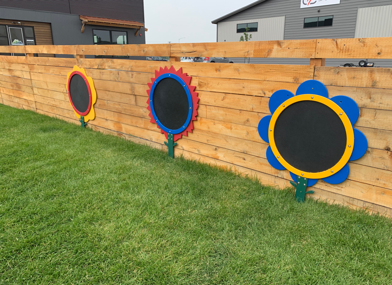 A wooden fence with three chalkboard flowers on it