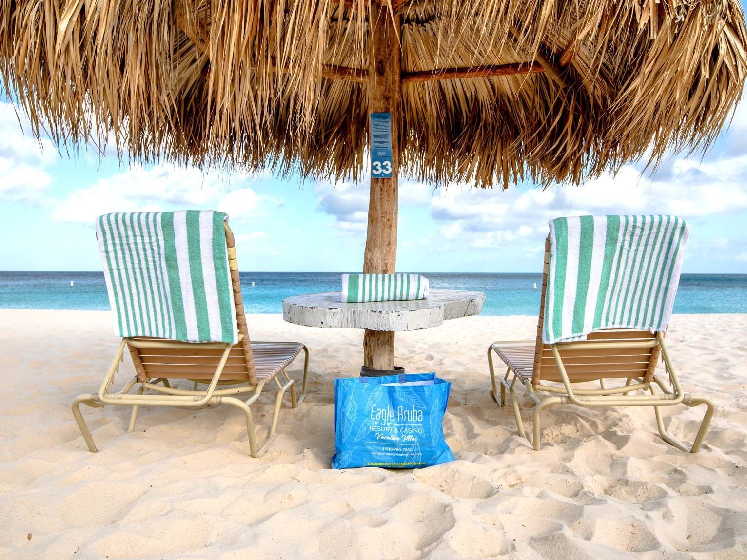 Two chairs and a table under an umbrella on a beach.