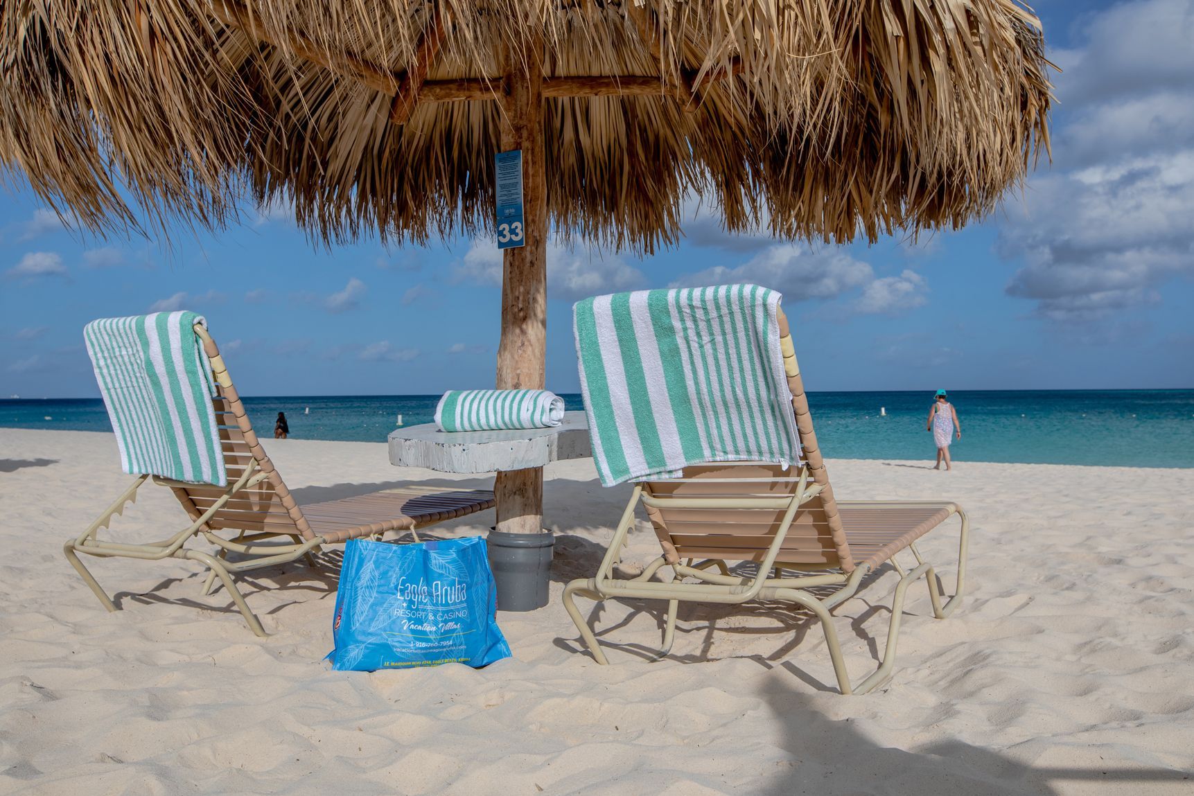 Two lounge chairs under an umbrella on a beach.