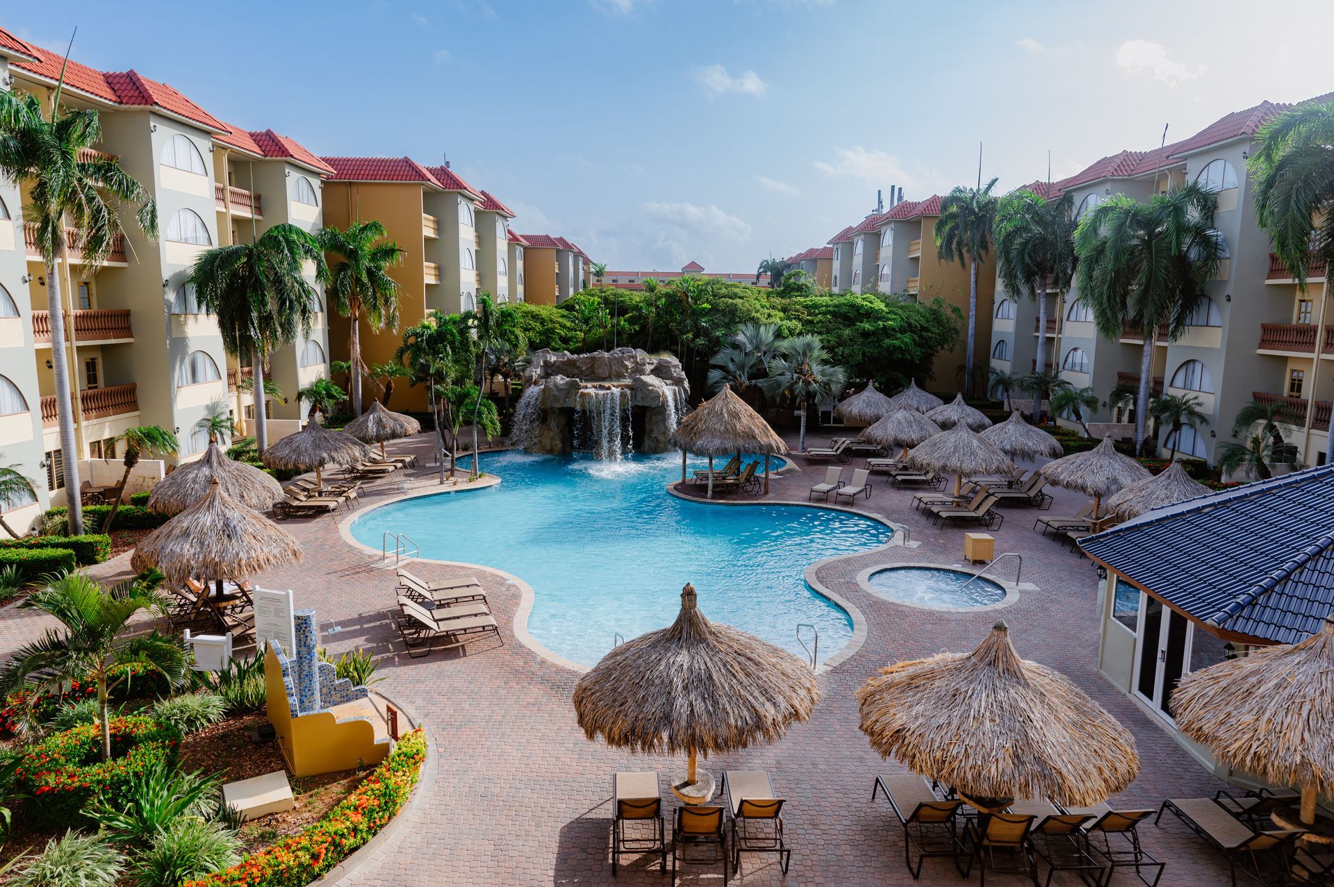 An aerial view of a large swimming pool surrounded by palm trees and umbrellas.