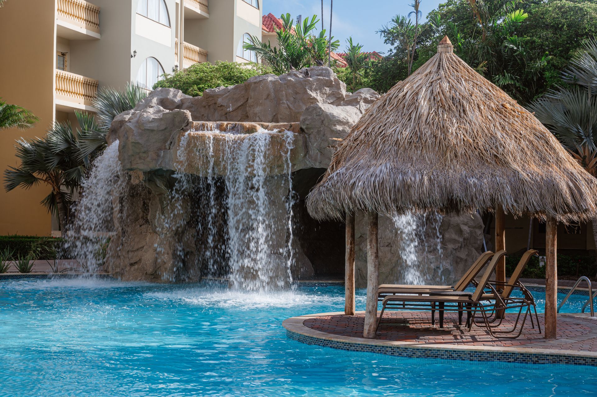 A swimming pool with a thatched hut and a waterfall in the background