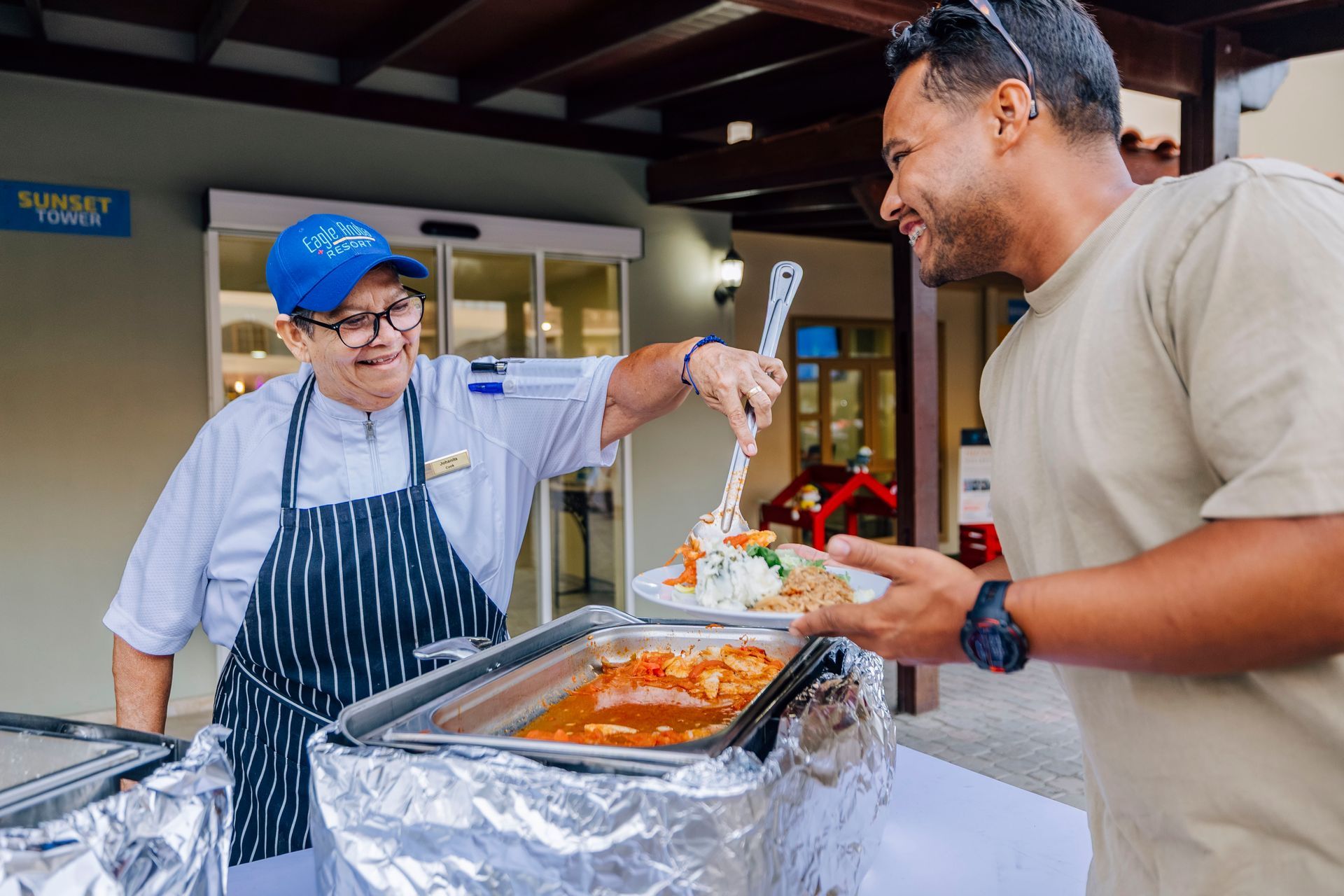 Chef serving a plate of food to a smiling man at an outdoor buffet.