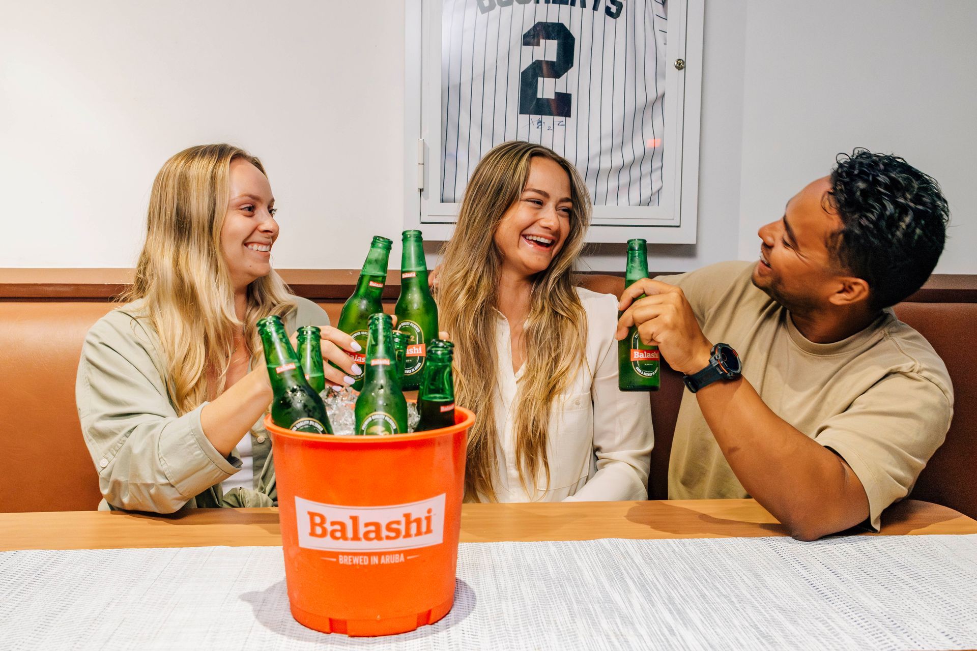 Three people toasting with green beer bottles from an orange bucket at a table.