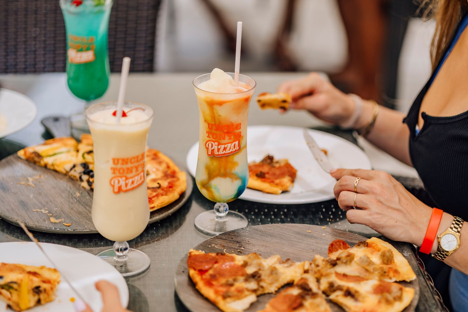 People eating pizza and drinking colorful cocktails at a restaurant.