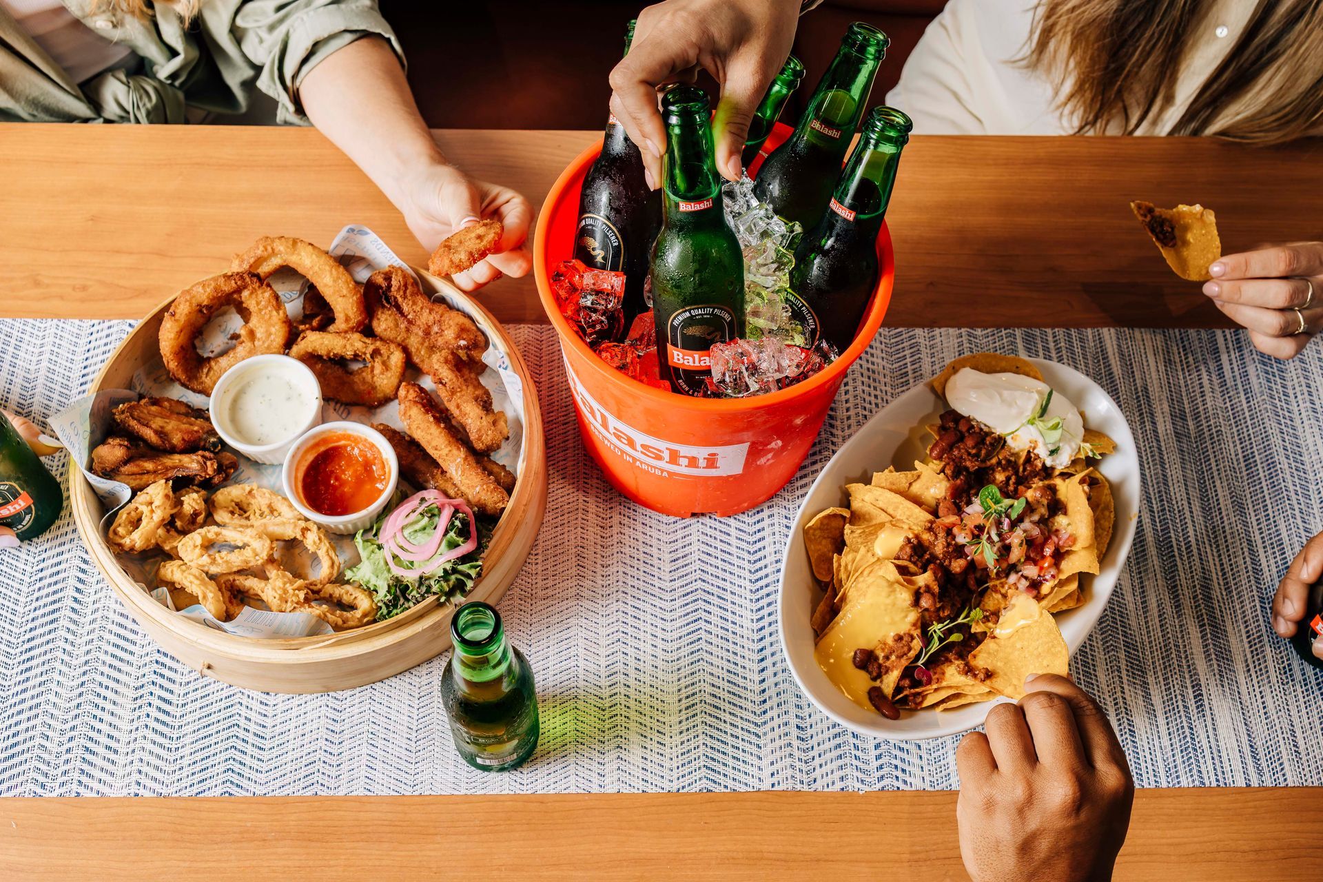 Group sharing food and drinks at a table: onion rings, nachos, beer bucket.