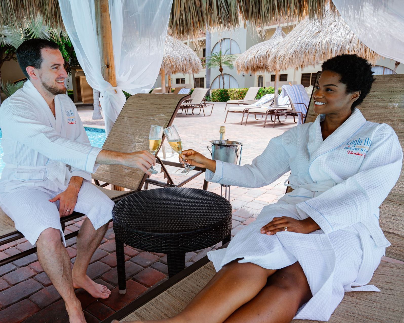 A man and a woman in bathrobes are toasting with champagne