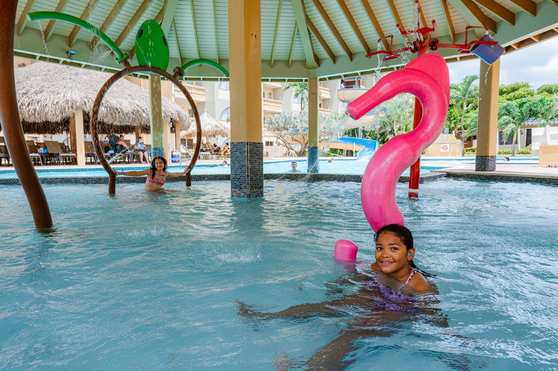 A little girl is swimming in a pool with a pink flamingo on her head.