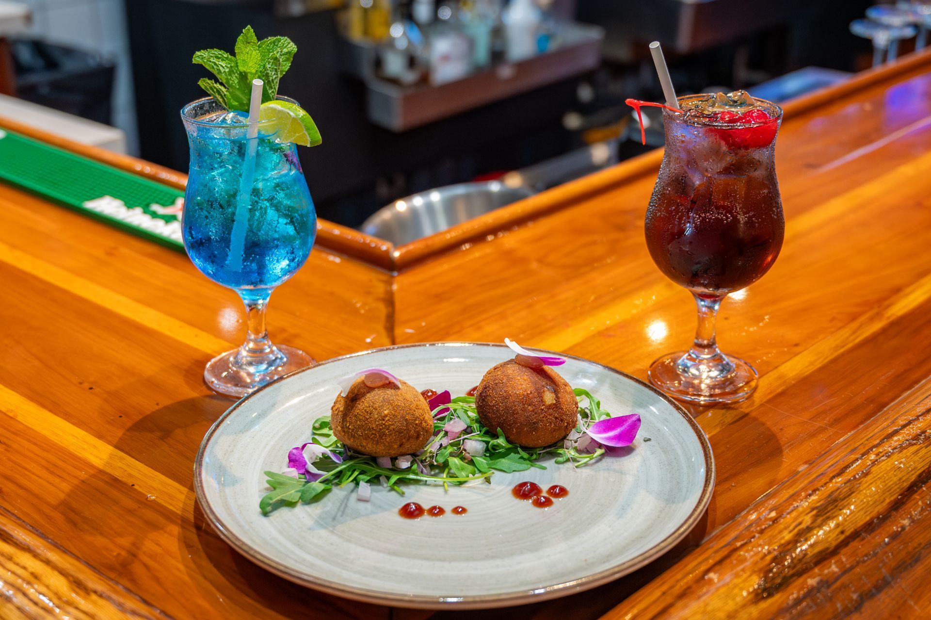A plate of food and two drinks on a wooden bar.