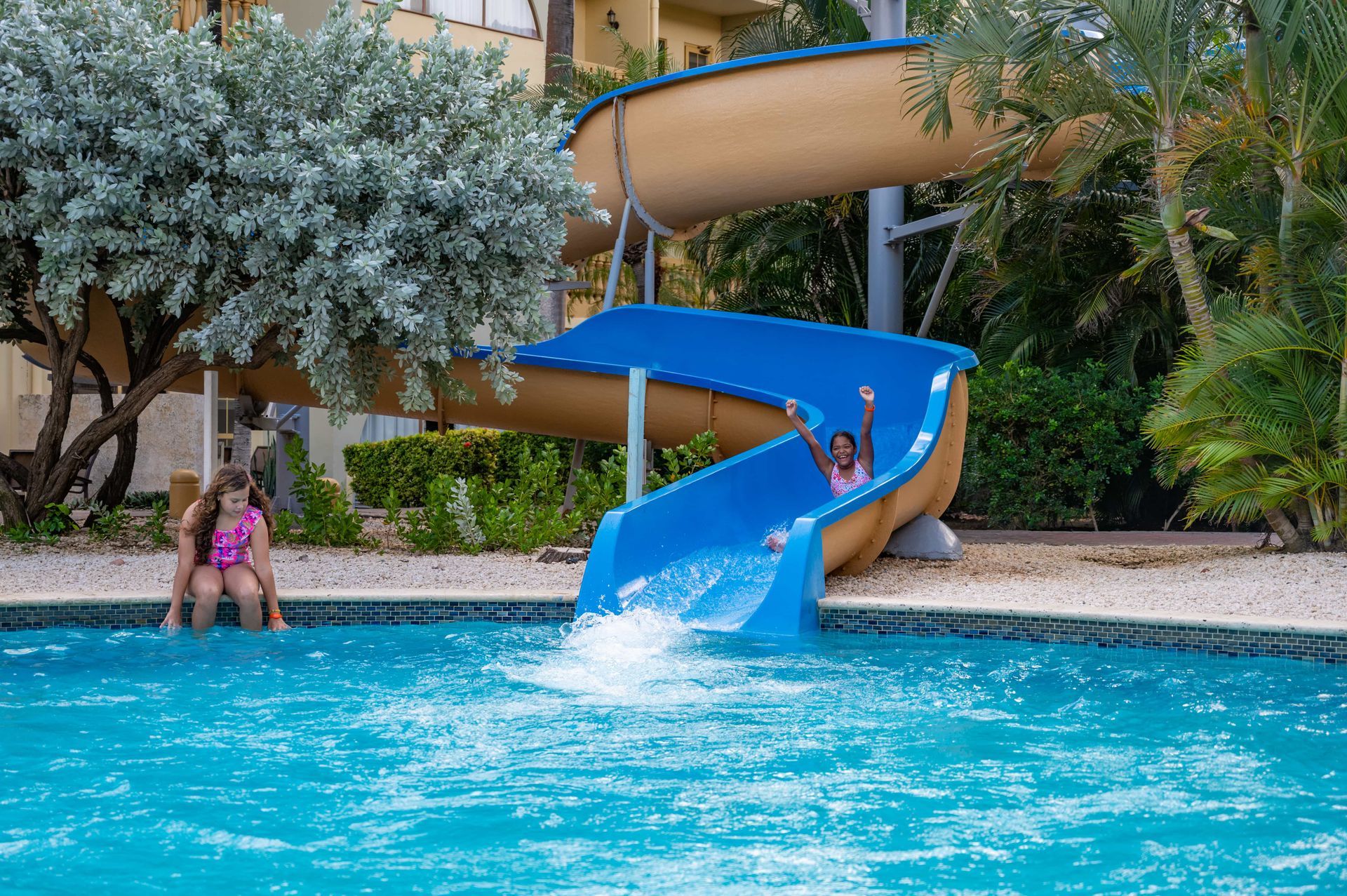 A girl is going down a water slide in a swimming pool.