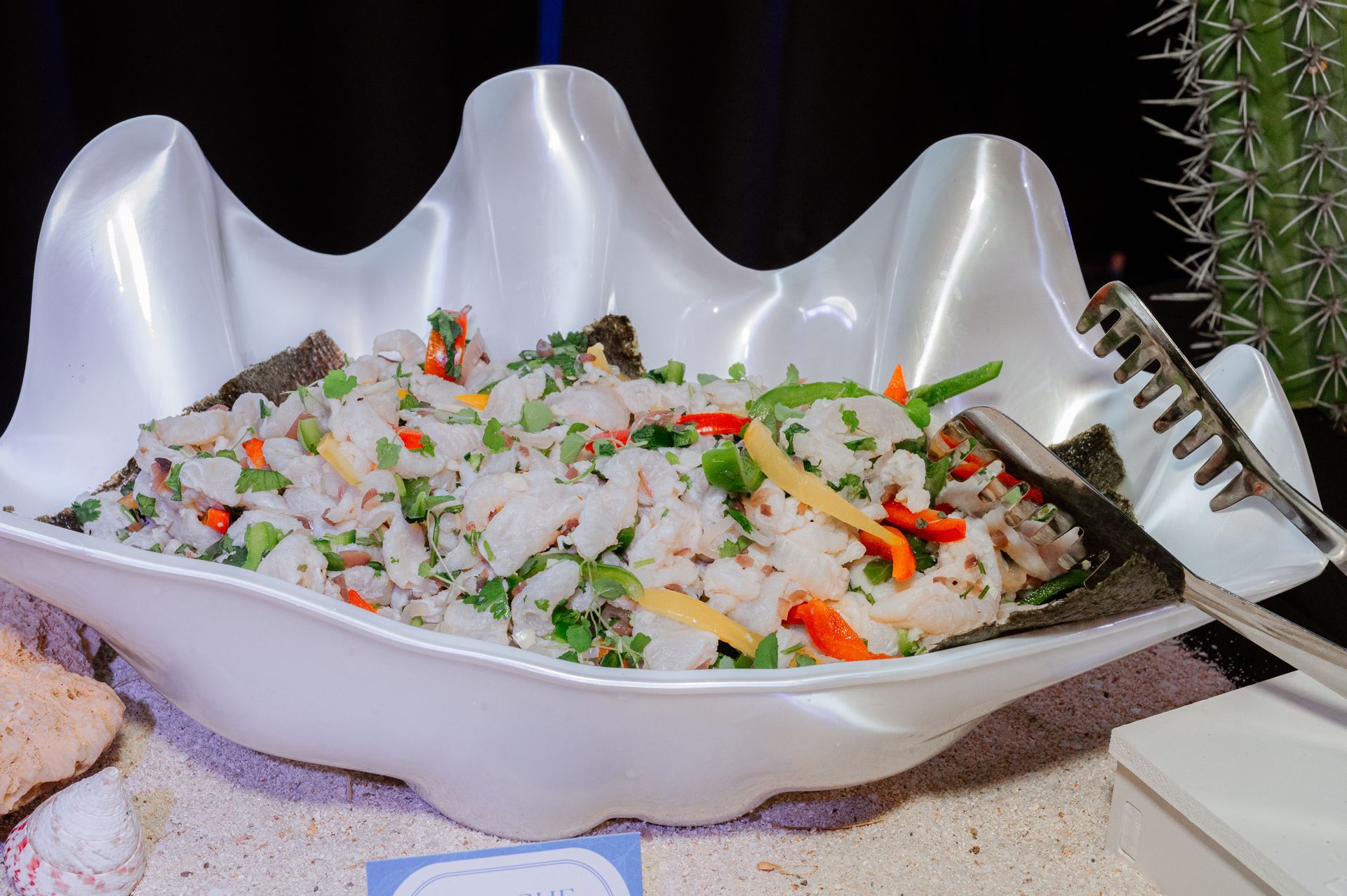 A large white bowl filled with food and tongs on a table.