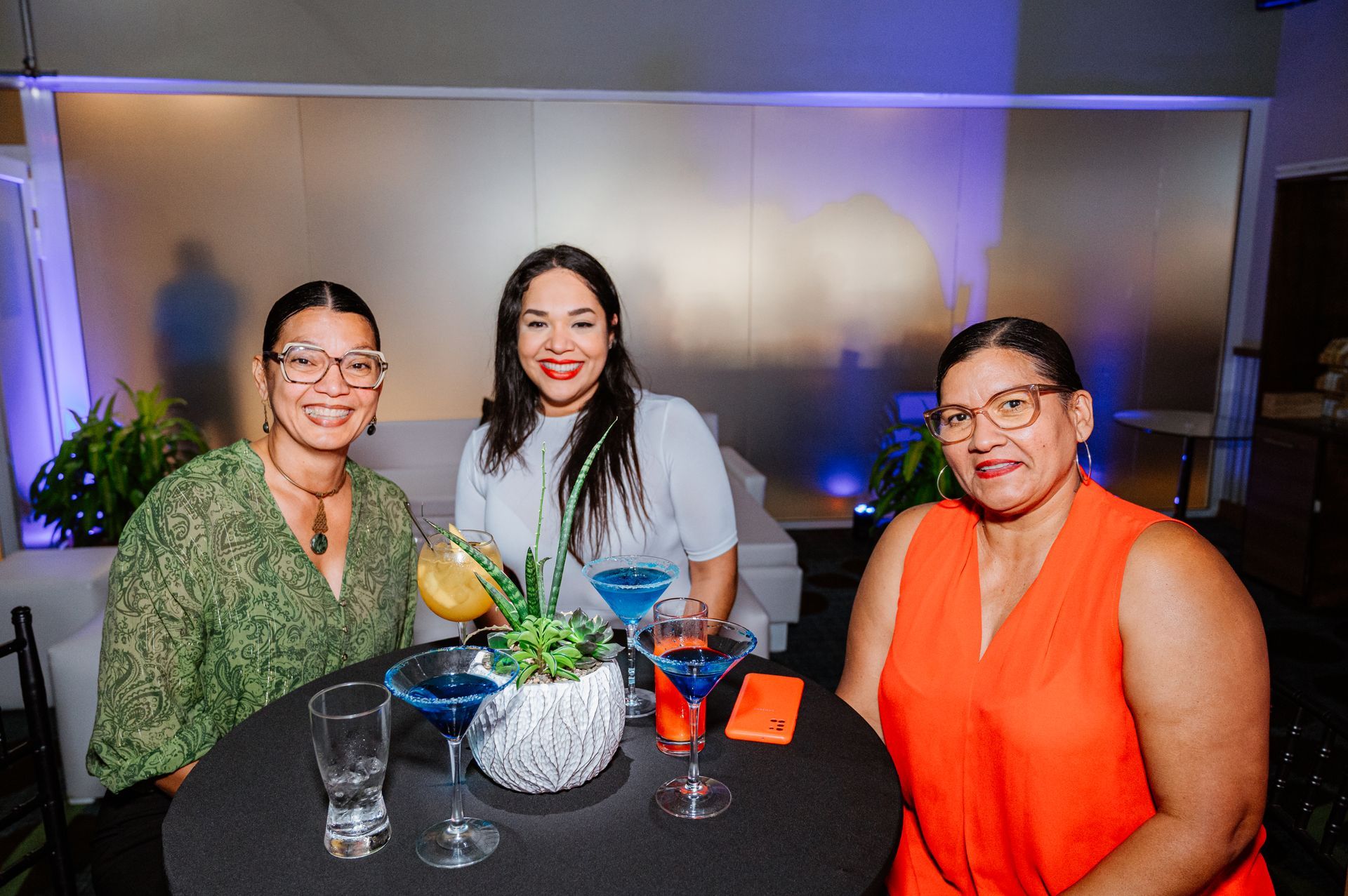 Three women are sitting at a table with drinks.