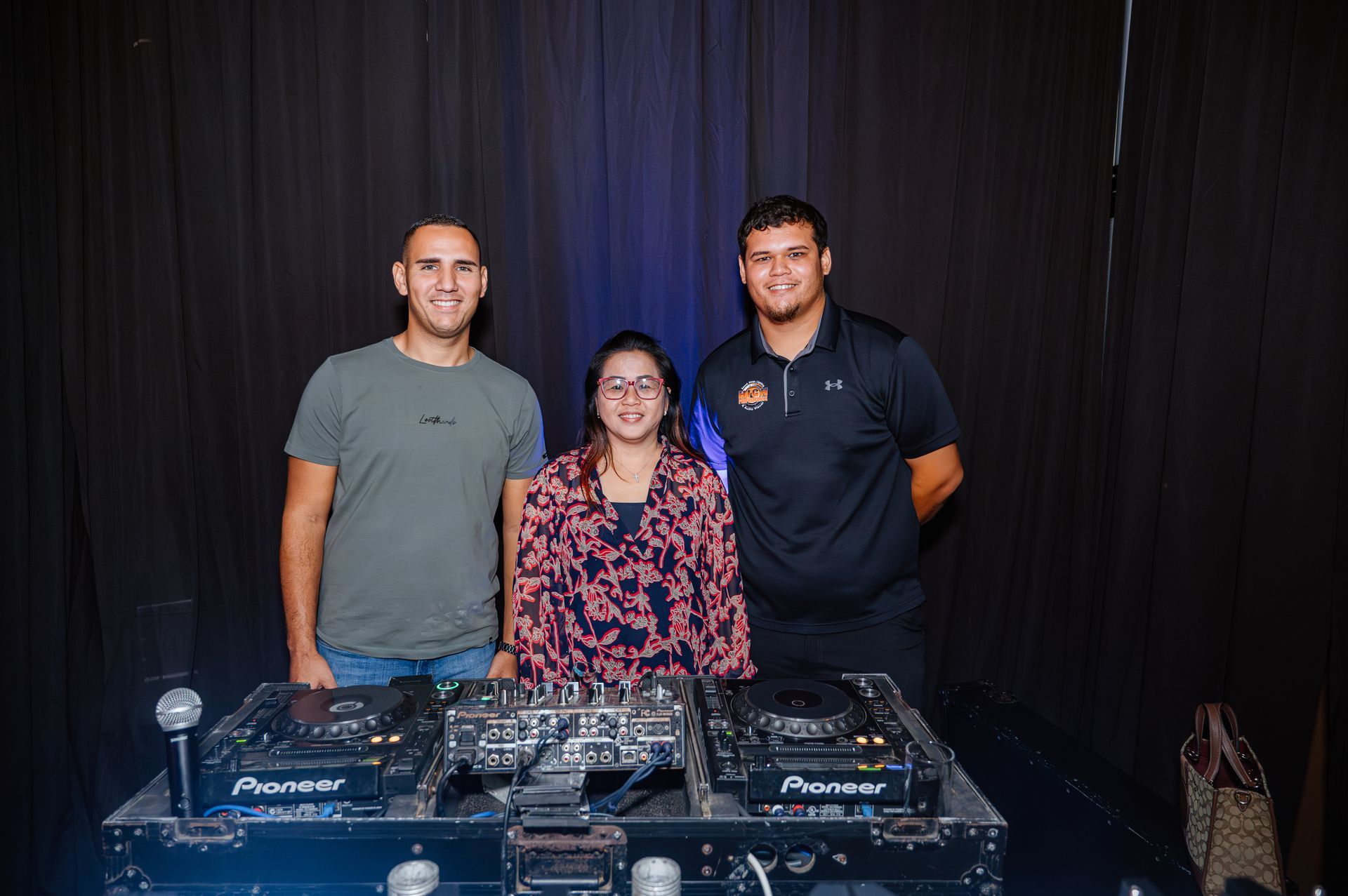Three people are posing for a picture in front of a dj booth.