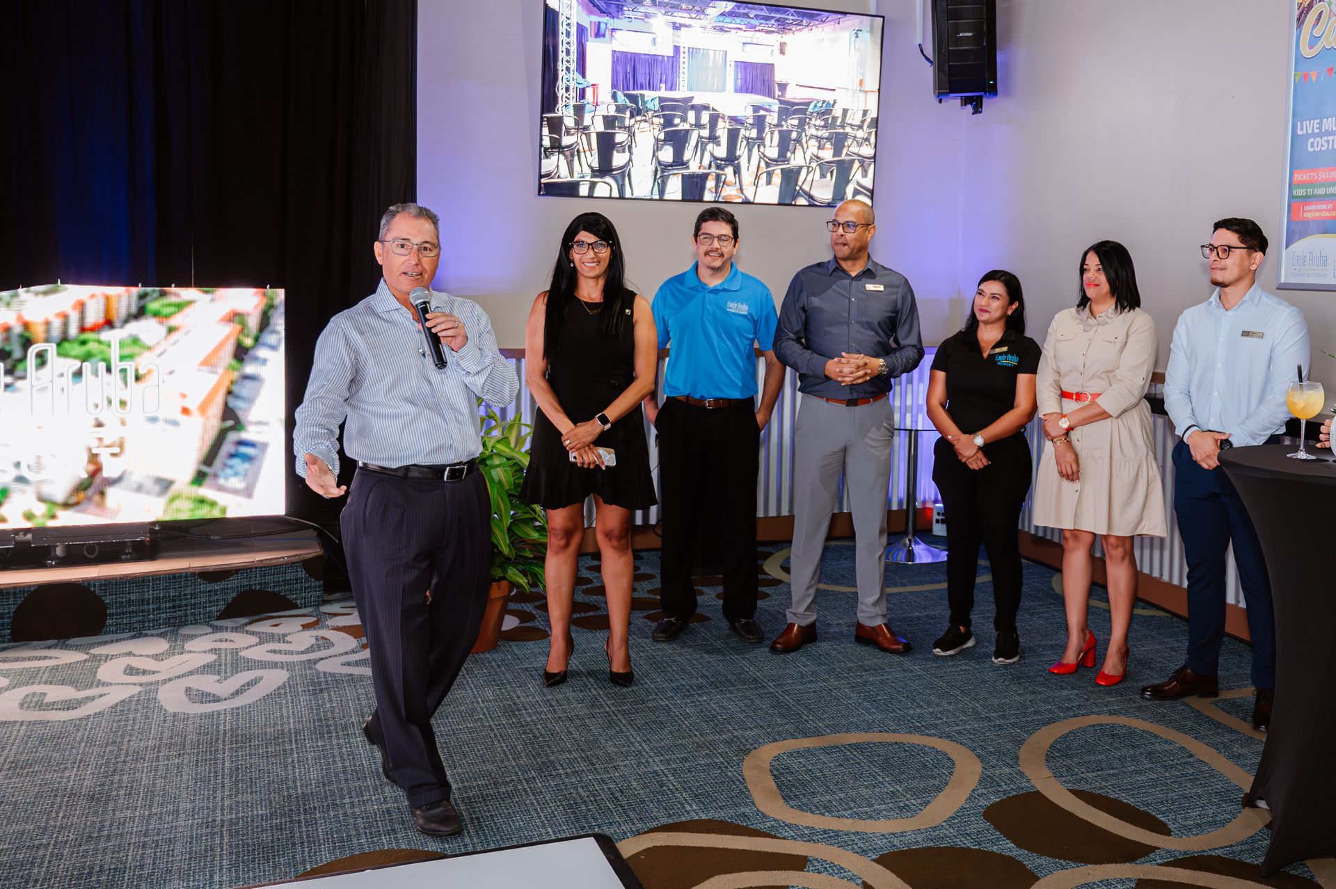 A group of people are standing in a room with a man standing in front of a microphone.