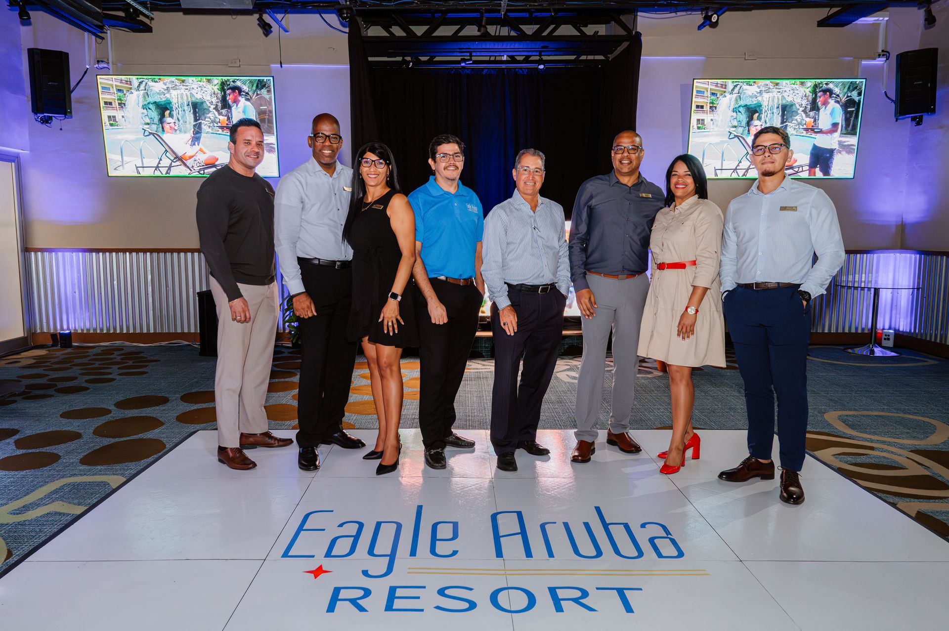 A group of people are posing for a picture in front of a sign that says eagle aruba resort.