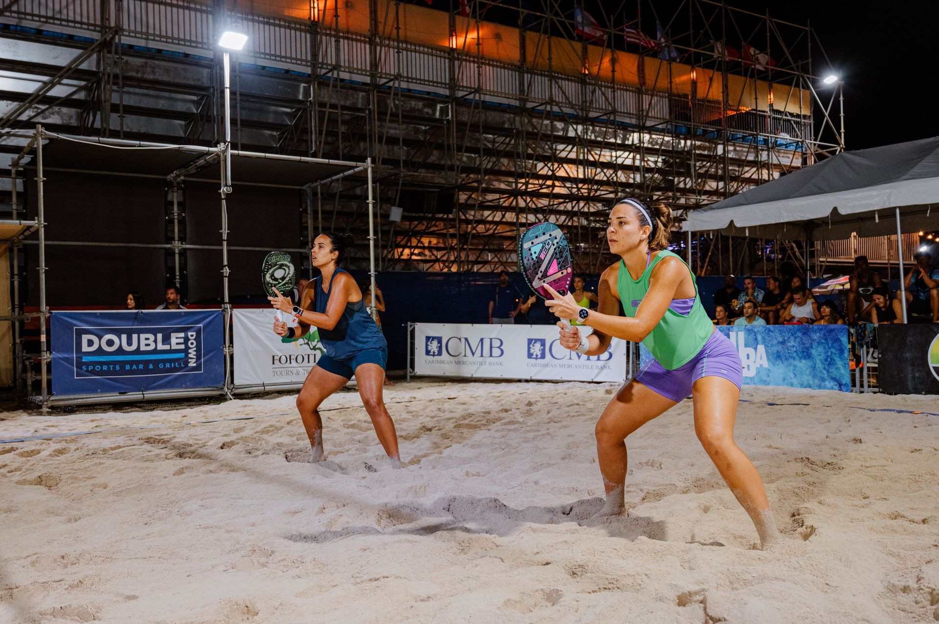 Two women playing beach tennis at night. One in green, one in blue.