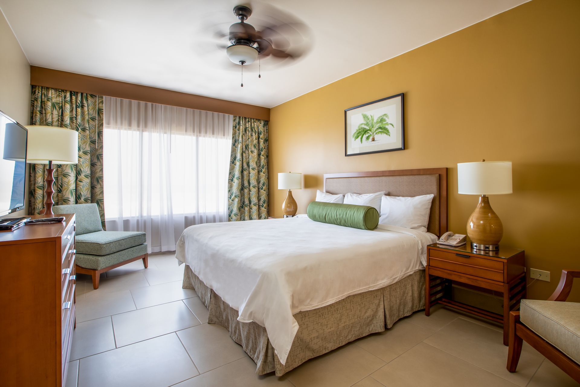 A hotel room with a king size bed and a ceiling fan.
