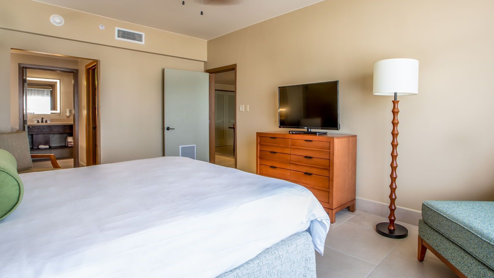 A hotel room with a bed , dresser , lamp and television.